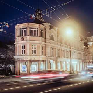 Schlossähnliches historisches Gebäude in der Dunkelheit hinter vorbeifahrenden Autos und Stromleitungen.