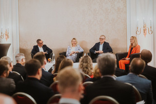 Elegant gekleidetes Publikum lauscht einer Podiumsdiskussion.