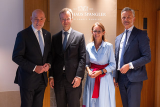 Eine Dame und drei Herren in eleganter Kleidung posieren lächelnd vor einem Rollup mit der Aufschrift "Bankhaus Spängler".