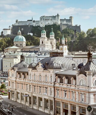 Stammhaus des Bankhaus Spängler in der Schwarzstraße 1 in 5020 Salzburg von außen. Die Fassade ist hellrosa, auffällig ist das Kuppeldach. Im Hintergrund sieht man die Festung Hohensalzburg sowie die Kuppeln des Salzburger Doms.