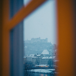 Blick durch ein Fenster auf eine verschneite mittelalterliche Festung und Altstadt.