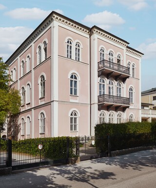 Bankgebäude des Bankhaus Spängler in der Schwarzstraße 17 in 5020 Salzburg von außen. Das Gebäude hat 3 Stockwerke, die Fassade ist hellrosa, 2 Balkone und viele Fenster sind ersichtlich.